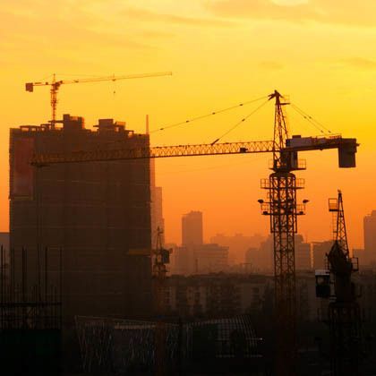 Silhouette of crane and buildings against orange sunset